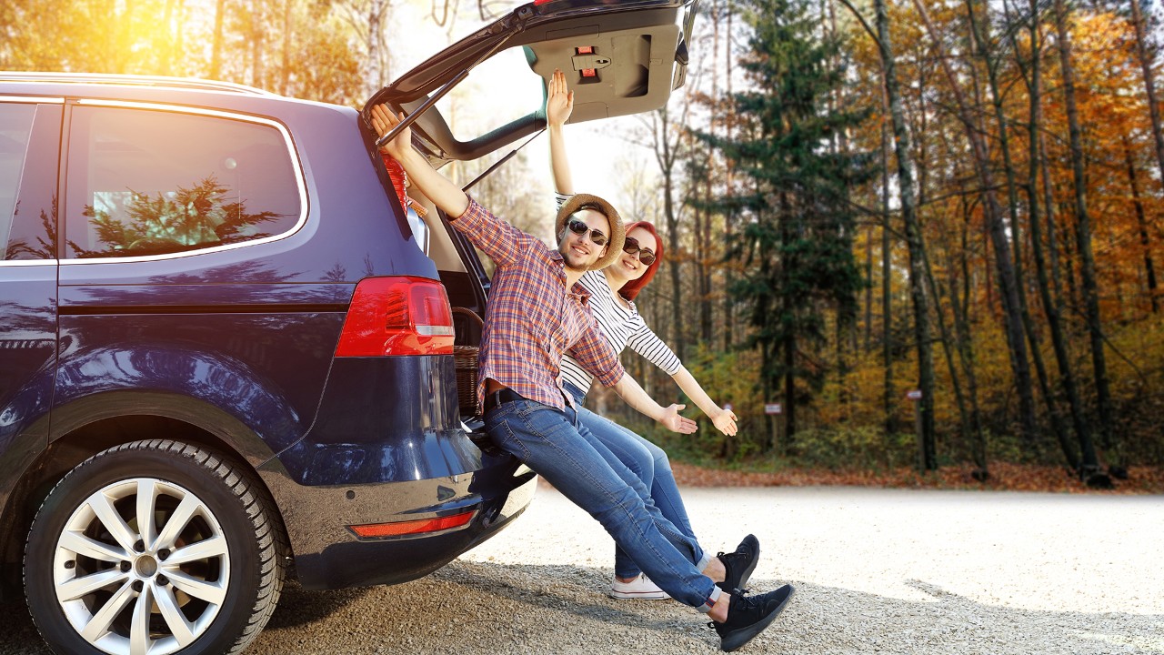 Deux voyageurs assis à l’arrière d’un monospace, les bras écartés et souriants.